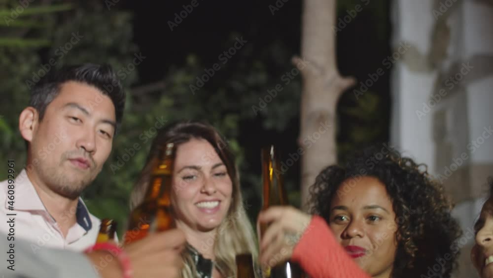 Diverse people clinking and raising bottles of beer up. Happy men and women having get together in backyard, spending evening together, laughing and drinking. Alcohol drinks, celebration concept Diverse people clinking and raising bottles of beer up. Happy men and women having get together in backyard, spending evening together, laughing and drinking. Alcohol drinks, celebration concept
