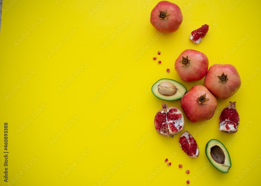 Four juicy and ripe pomegranates and cut cavocado on yellow background. Fruits contain many vitamins. Fresh fruits: good for body. food for diet. top view. place for text Four juicy and ripe pomegranates and cut cavocado on yellow background. Fruits contain many vitamins. Fresh fruits: good for body. food for diet. top view. place for text