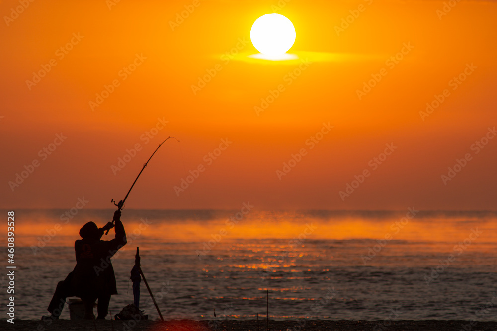 Fisherman fishing in the Sea or Ocean beach during sunrise. Swinging a rod