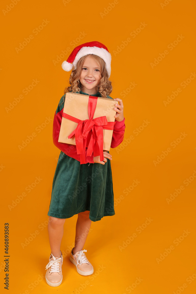 a beautiful blonde girl in a red and green Santa Claus hat dress holds a gift box on a yellow background