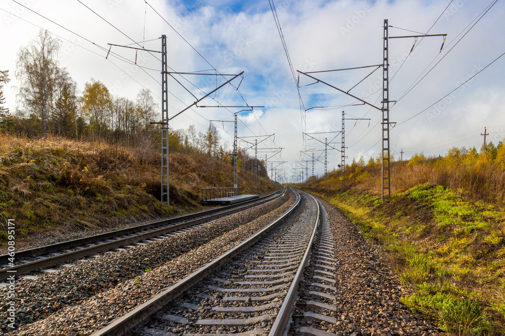Rural autumn landscape on empty railroad in Siberia. Railroad tracks receding into the distance. Industrial landscape with wooden railway platform
