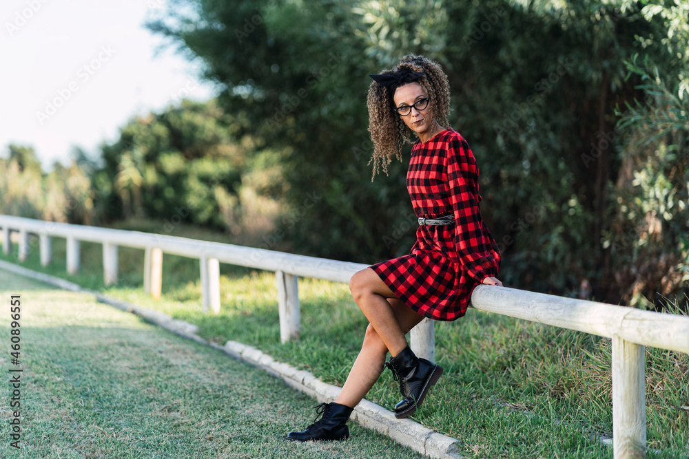 Chica delgada con el pelo rizado y vestido de cuadros rojos y negros en parque posando Chica delgada con el pelo rizado y vestido de cuadros rojos y negros en parque posando