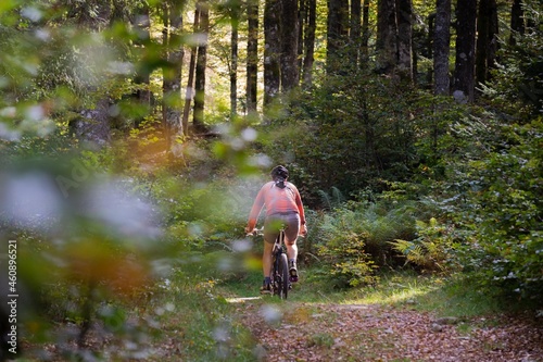 A person riding a bike in the woods. Red shirts and green leaves. 