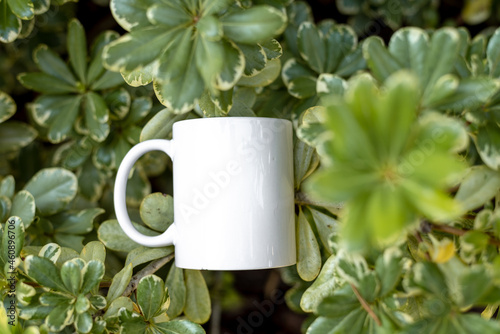 White porcelain mug cup isolated on green plants background with copy space. Mock up for design. 
