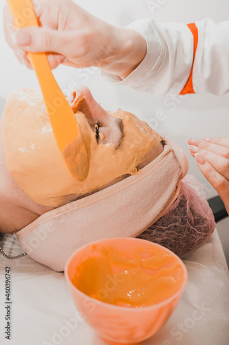 Using a gold mask in cosmetology, a woman at a beautician applying a gold mask on her face.