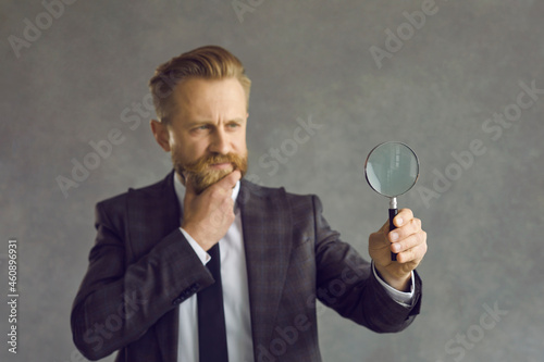 Serious pensive thoughtful man businessman in suit frowning face scratching beard looking through magnifying glass. Research investigation, analysis and search business problem solution concept