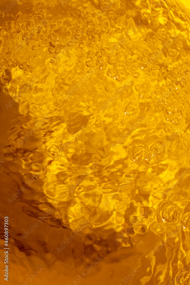 blurred yellow abstract background of reflection of running water with bubbles, top view, vertical.