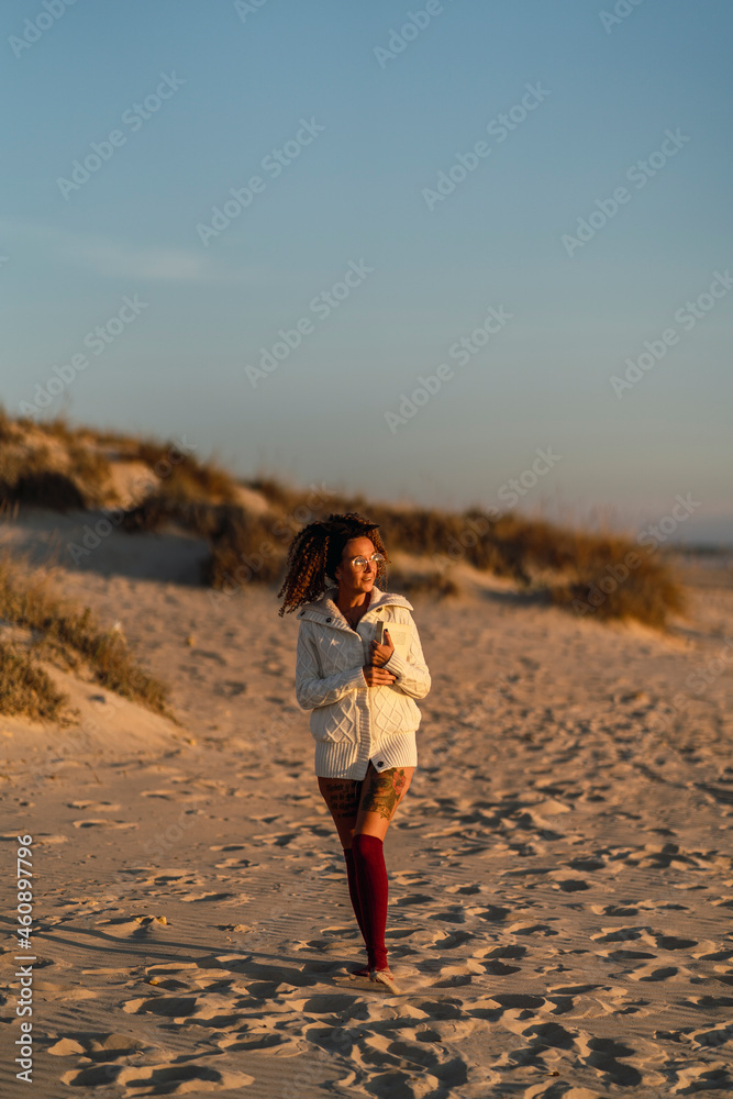 Chica delgada con el pelo rizado en la playa al atardecer