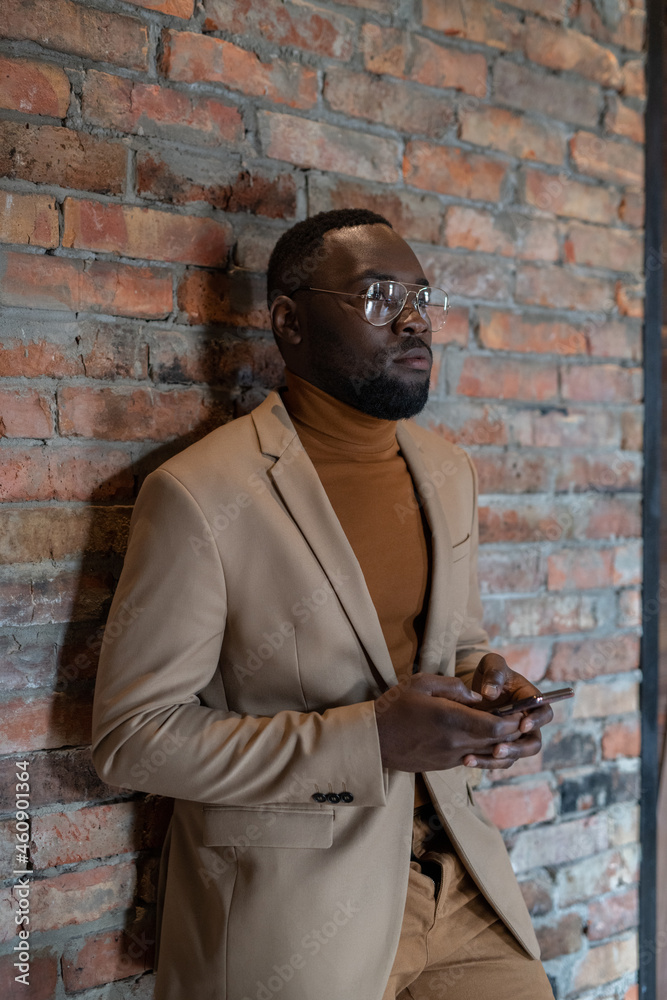 Obraz premium Young serious businessman with smartphone waiting for someone against brick wall