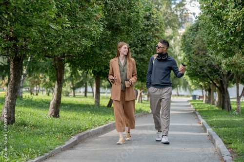 Fototapeta Naklejka Na Ścianę i Meble -  Two young colleagues in casualwear walking in large public park on summer day