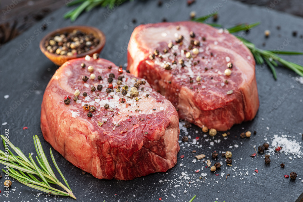 Raw Ribeye steaks with salt and herbs on grey board. Top view.