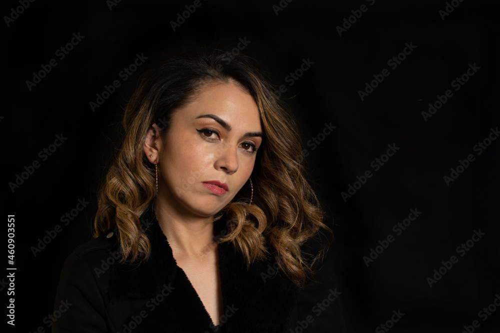 Dramatic portrait of a Latina woman with serious or arrogant expression looking straight into the camera over black background Dramatic portrait of a Latina woman with serious or arrogant expression looking straight into the camera over black background
