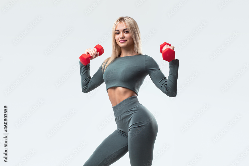 A beautiful model in sportswear with dumbbells looks at the camera. A beautiful model in sportswear with dumbbells looks at the camera.