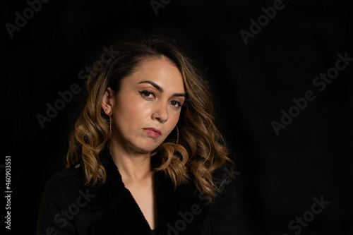 Dramatic portrait of a Latina woman with serious or arrogant expression looking straight into the camera over black background