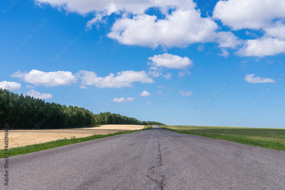 Paved road in the field and clouds in the blue sky.