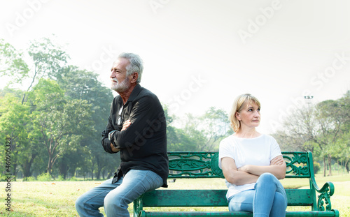 Offended mature man and woman sitting on different sides of bench outdoors at park. Old man and his wife ignoring and not speaking each other after conflict or fight. Relationship problems and upset.