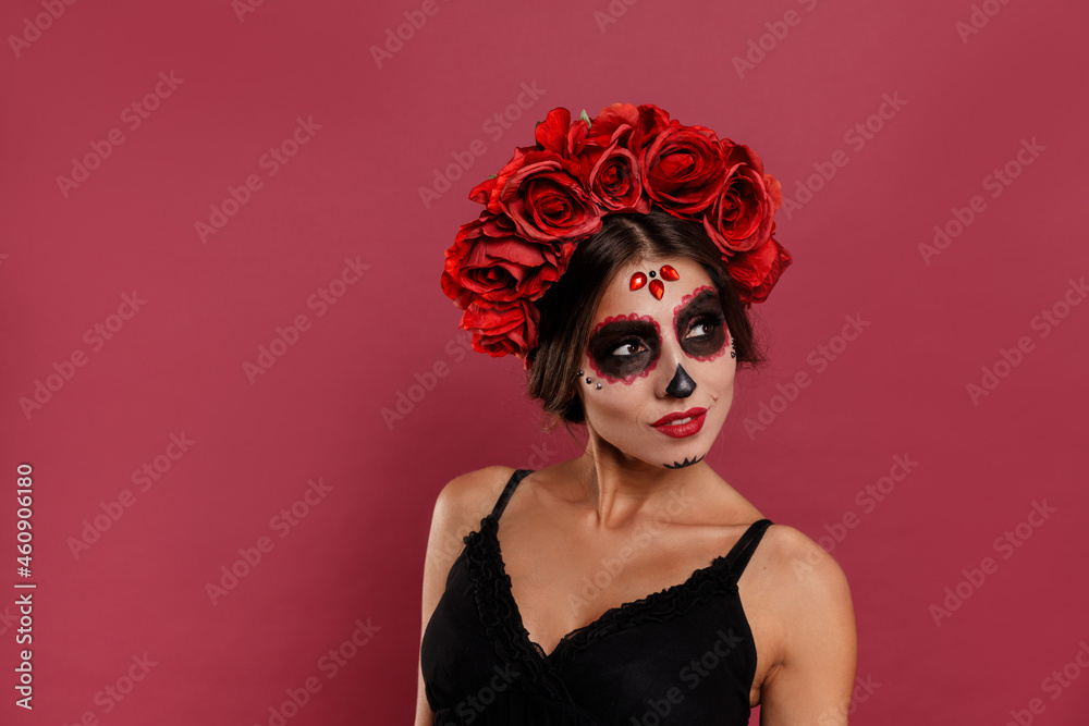 Beautiful girl in la muerta attire and skull make up looking to camera during halloween
