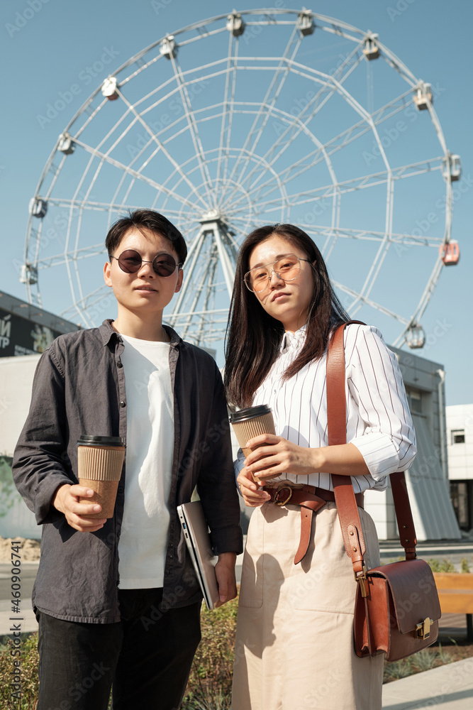 Young Chinese students standing against Ferris wheel and looking at camera Young Chinese students standing against Ferris wheel and looking at camera