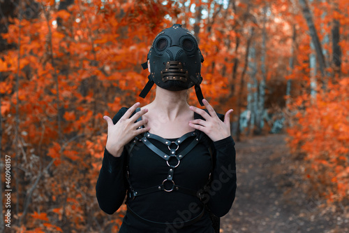a girl in a bdsm costume and a black mask in a red forest.an idea for halloween.