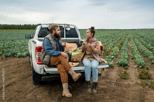 Two young farmers with mugs having tea at break after working at cabbage field photo