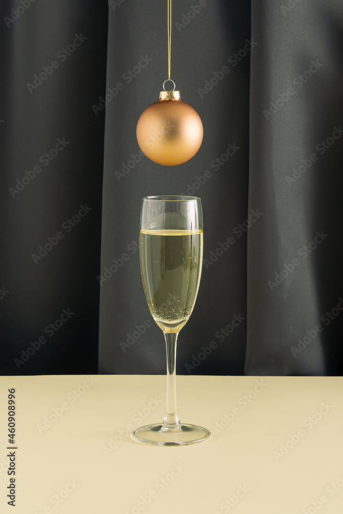 Creative, elegant Christmas .arrangement with golden rose bauble and glass of .champagne on a gray curtain backgorund. Minimal New Year or party concept.