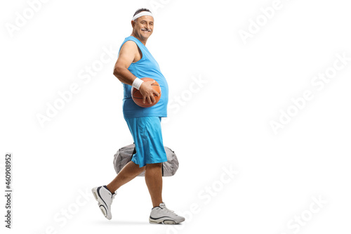 Full length profile shot of a mature man walking and carrying a basketball and a sports bag