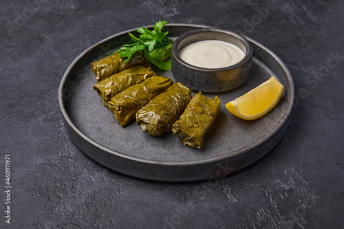Traditional Middle Eastern dish dolma or sarma, with parsley, saucepan with sour cream and lemon in black plate on dark wood background. Close up