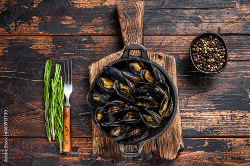 Mussels cooked with white wine sauce in a pan with herbs. Dark wooden background. Top view