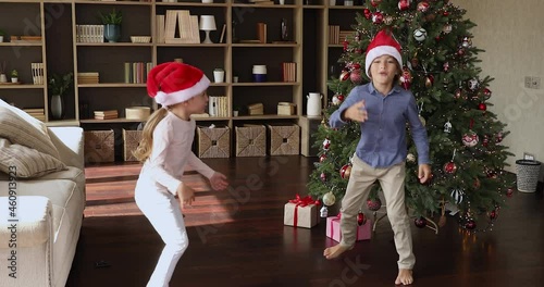 It is Christmas. Overjoyed preteen kids elder brother younger sister jump laugh go crazy meet New Year holiday near big beautiful fir tree at home. Excited little children having fun celebrating Xmas