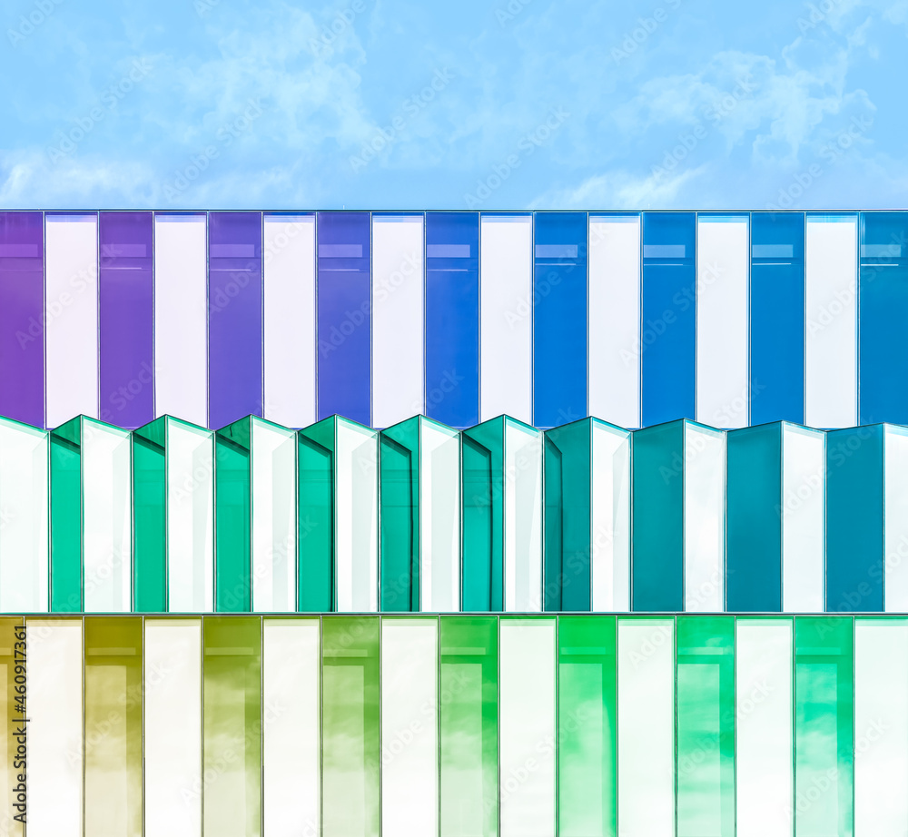Abstract image of modern gradient colorful glass building. Architectural exterior futuristic art and detail. Closeup of geometric structure, multicolored facades. Skyscraper with clouds reflection. Abstract image of modern gradient colorful glass building. Architectural exterior futuristic art and detail. Closeup of geometric structure, multicolored facades. Skyscraper with clouds reflection.