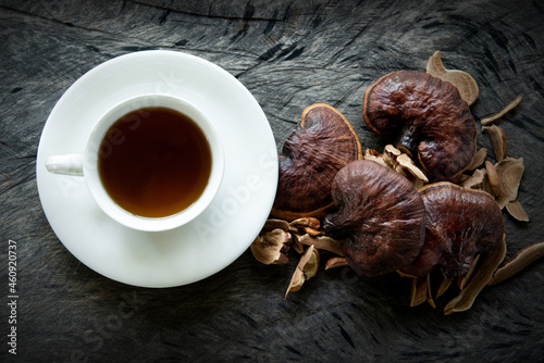 Cup of reishi tea and fresh Lingzhi mushroom with slice on dark wooden floor. (Ganoderma Lucidum). Chinese traditional medicine and nutritive value. photo