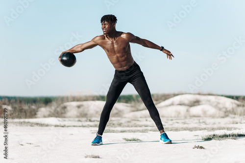 Fitness African American man doing workout twist exercise with medicine ball weight, outdoors on nature