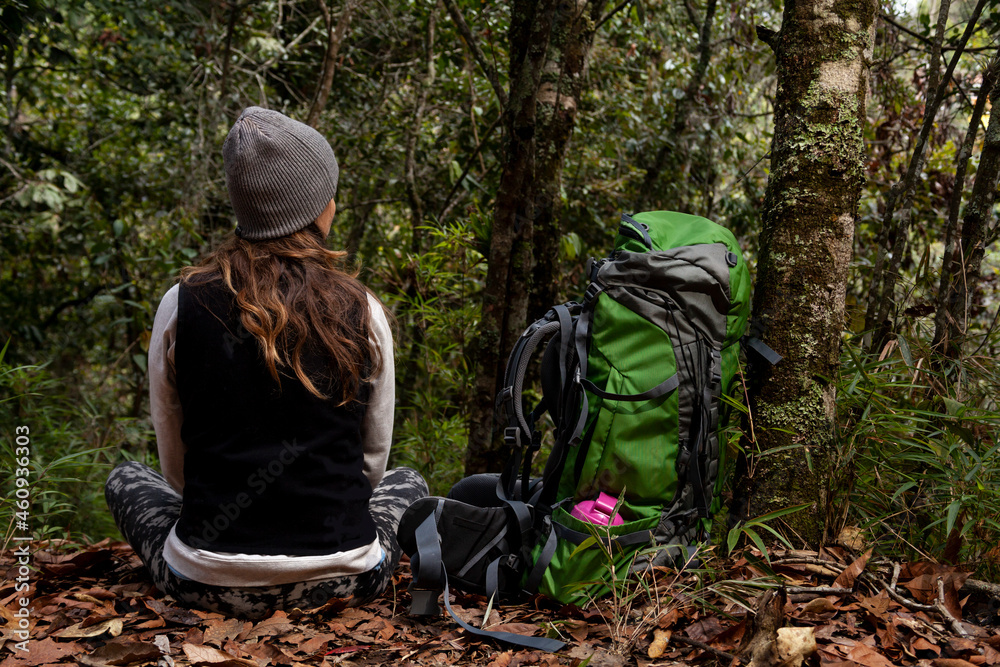 Woman on an adventure trip through a forest with dry leaves floor of Colombia, next to her a green backpack