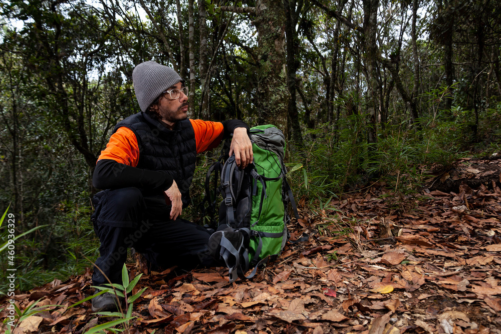 Man on an adventure trip through a forest with dry leaves floor of Colombia, next to her a green backpack Man on an adventure trip through a forest with dry leaves floor of Colombia, next to her a green backpack