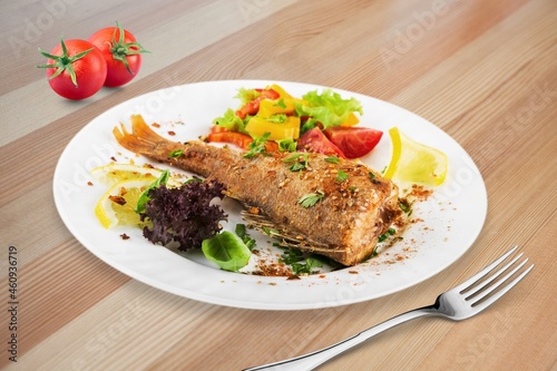 Tasty fish dish in a bowl, fork on a wooden table. Low calories healthy eating