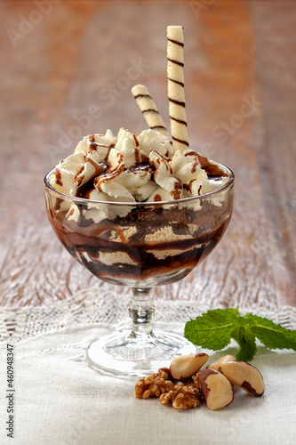 Sorvete de creme com calda de chocolate e cobertura de creme chantilly e tubetes de wafer crocante, no fundo de madeira. photo