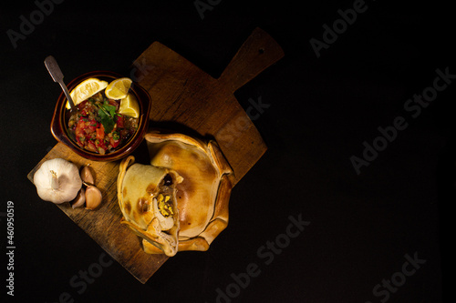 top view of a table with empanadas and a bowl of pebre on a black background, traditional Chilean dish photo
