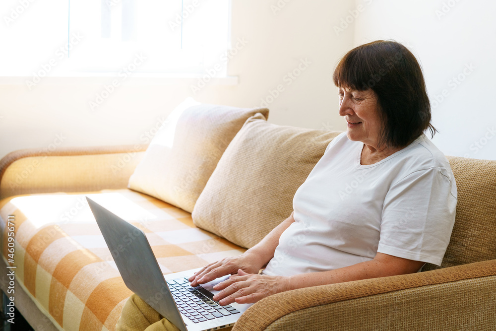 Elderly woman smiling 60s, sitting at home on couch, holding laptop. Senior happy business woman using computer technology, work, conversation, pastime on social networks internet, e-commerce. Elderly woman smiling 60s, sitting at home on couch, holding laptop. Senior happy business woman using computer technology, work, conversation, pastime on social networks internet, e-commerce.