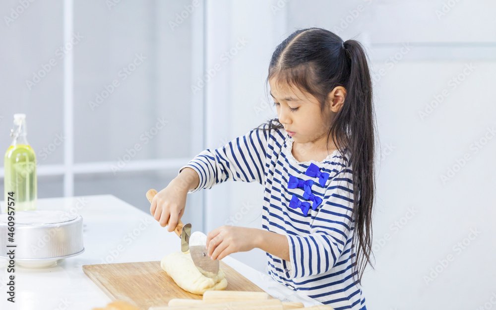 Young little Asian girl kneading and cutting dough to make pastry in modern kitchen for cooking and baking concept Young little Asian girl kneading and cutting dough to make pastry in modern kitchen for cooking and baking concept