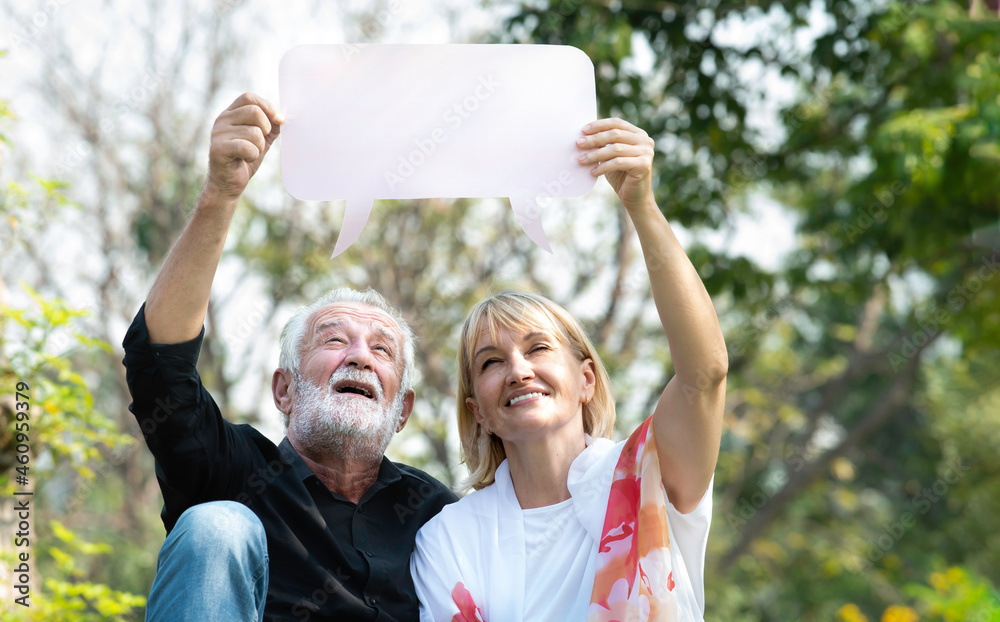 Portrait of senior caucasian couple displaying blank banner ad in the park. Happy elderly couple holding empty white board plank in a summer park. Mature retired couple with blank banner mock up.