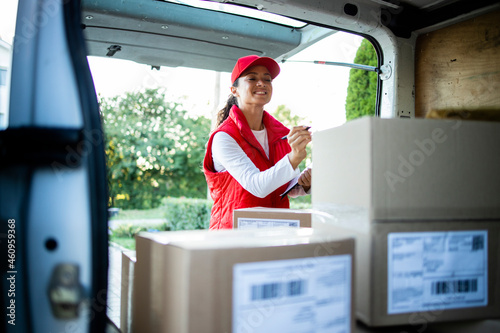 Fotografi Portrait of hardworking female courier arranging packages before delivery