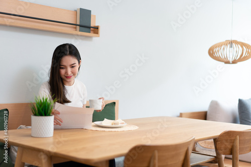 Living room concept a pretty lady holding a paper to read while another hand holding a cup of caffeine beverage in the living room