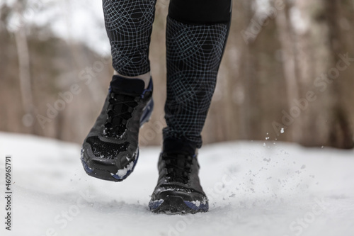 Winter running shoes woman training cardio outdoors jogging on white snow in cold weather. Closeup of feet wearing fitness footwear.