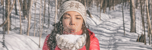 Winter Asian young woman blowing on snow for fun playing outdoor in nature forest. happy girl banner panoramic wearing cold weather accessories.