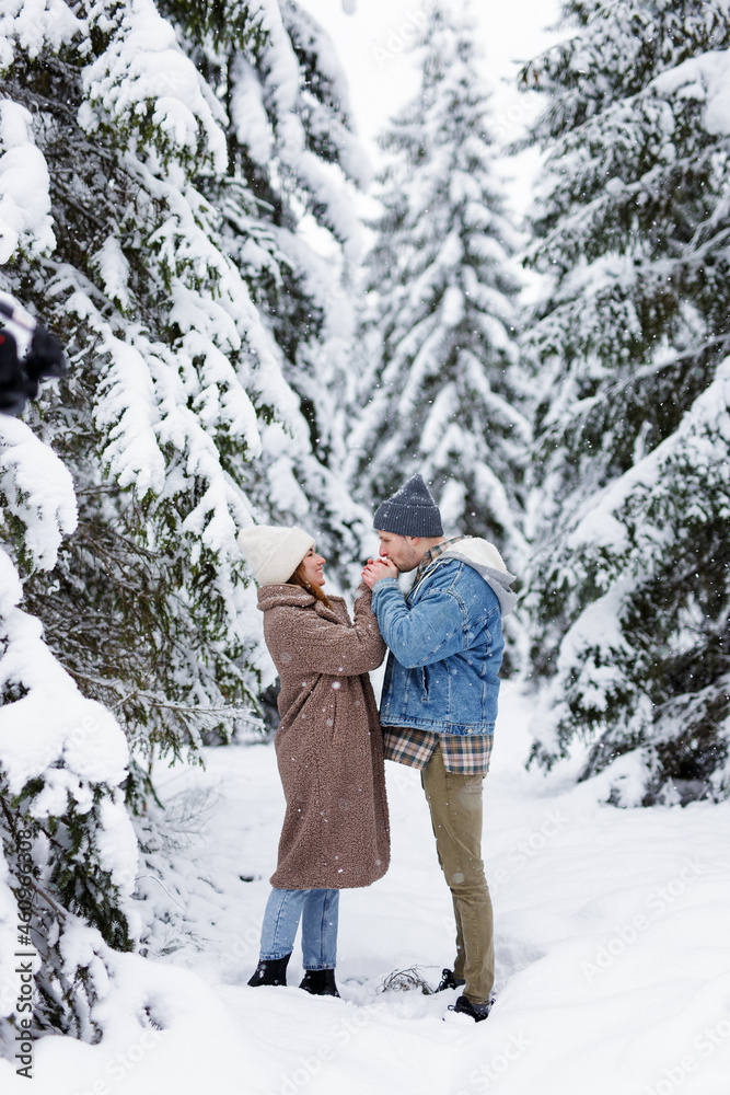 lovely couple standing in winter forest, holding hands and blowing to keep warm in the cold