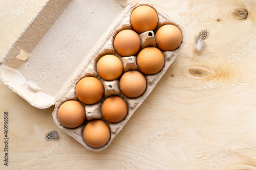 Raw brown chicken eggs in cardboard box on wooden background, top view