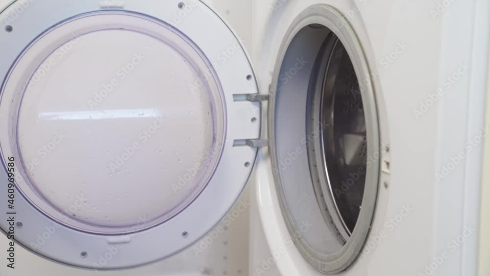 a woman puts dirty clothes in a washing machine and a capsule. a woman puts dirty clothes in a washing machine and a capsule.