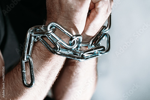 Repented man prisoner with his hands shackled in chains on a dark gray background.Closeup.