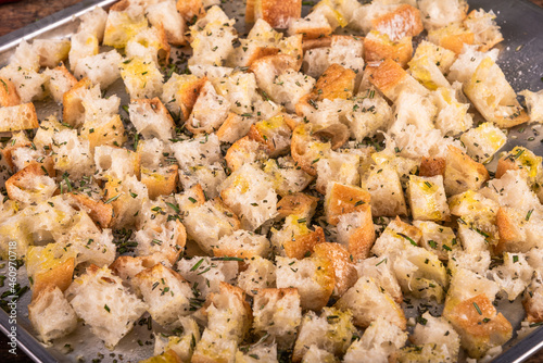 Ciabatta cubes prepared for baking with olive oil and rosemary on a baking sheet, close-up, making croutons.