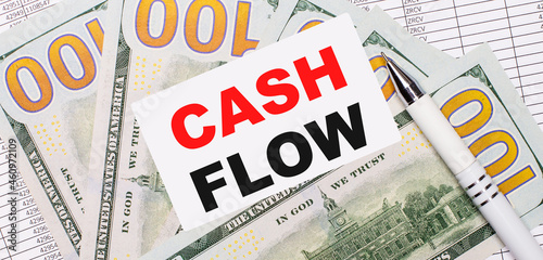 Against the background of reports and dollars - a white pen and a card with the text CASH FLOW. Business concept